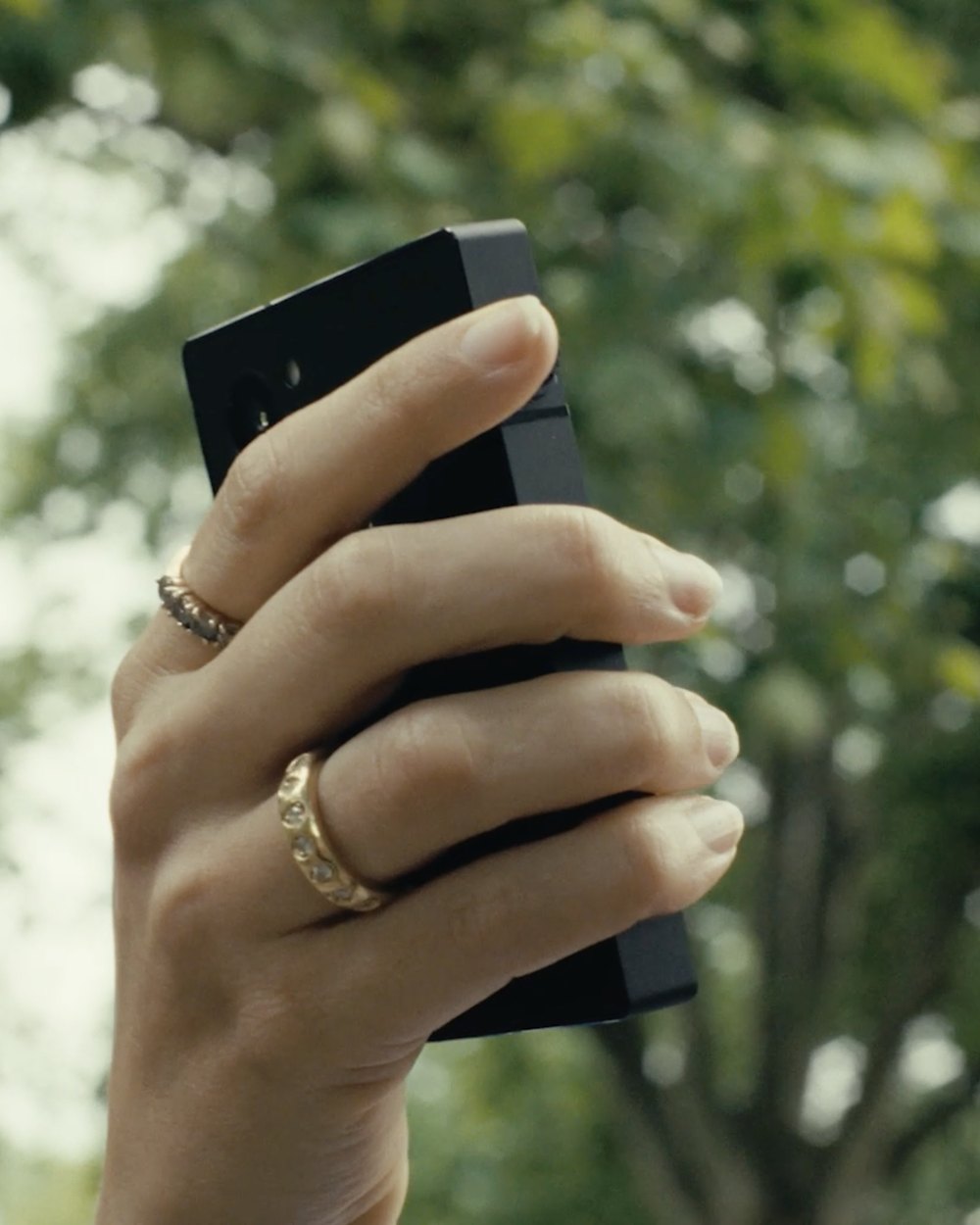 A hand holding a Light Phone up against trees